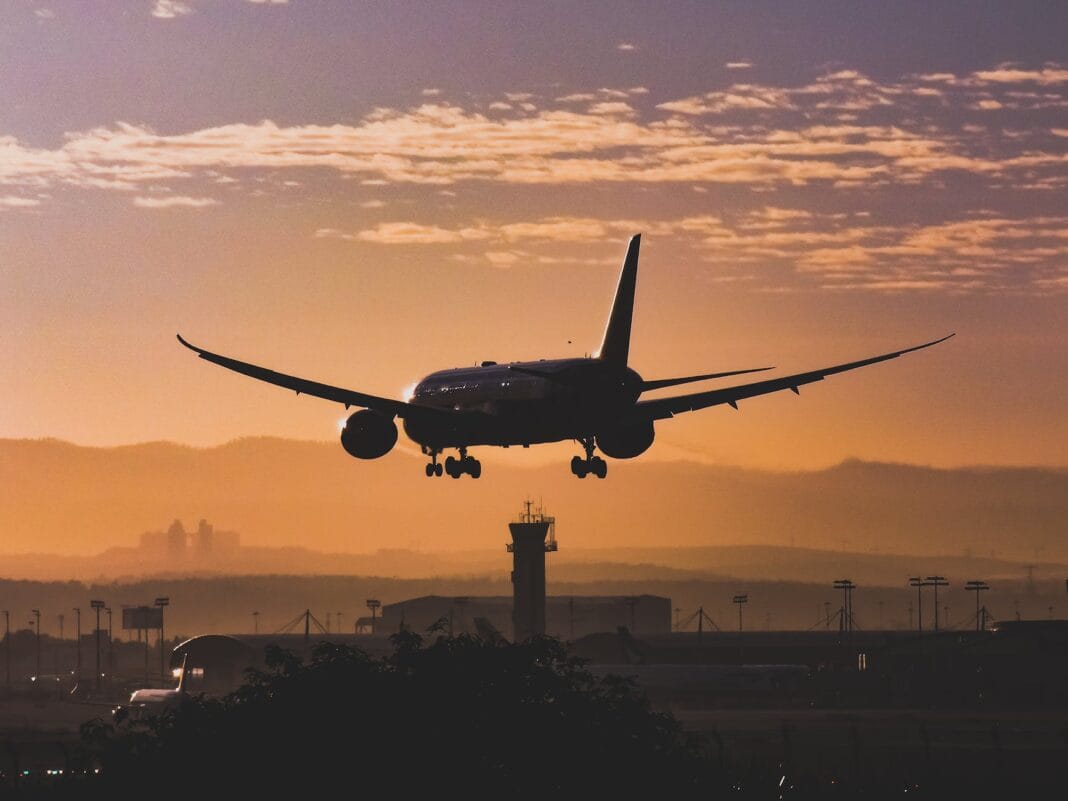 white passenger plane flying over the city during sunset